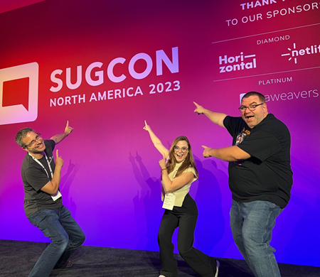 Three SearchStax employees point at SUGCON banner during SUGCON NA 2023.
